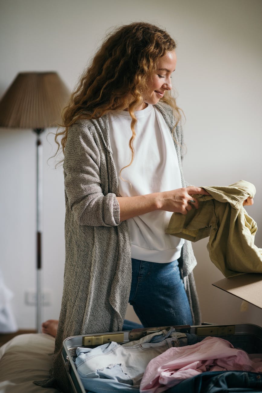 cheerful young female packing suitcase in bedroom while moving house